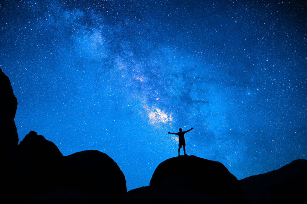 Shadow of a man on a mountain under a bright blue night sky.